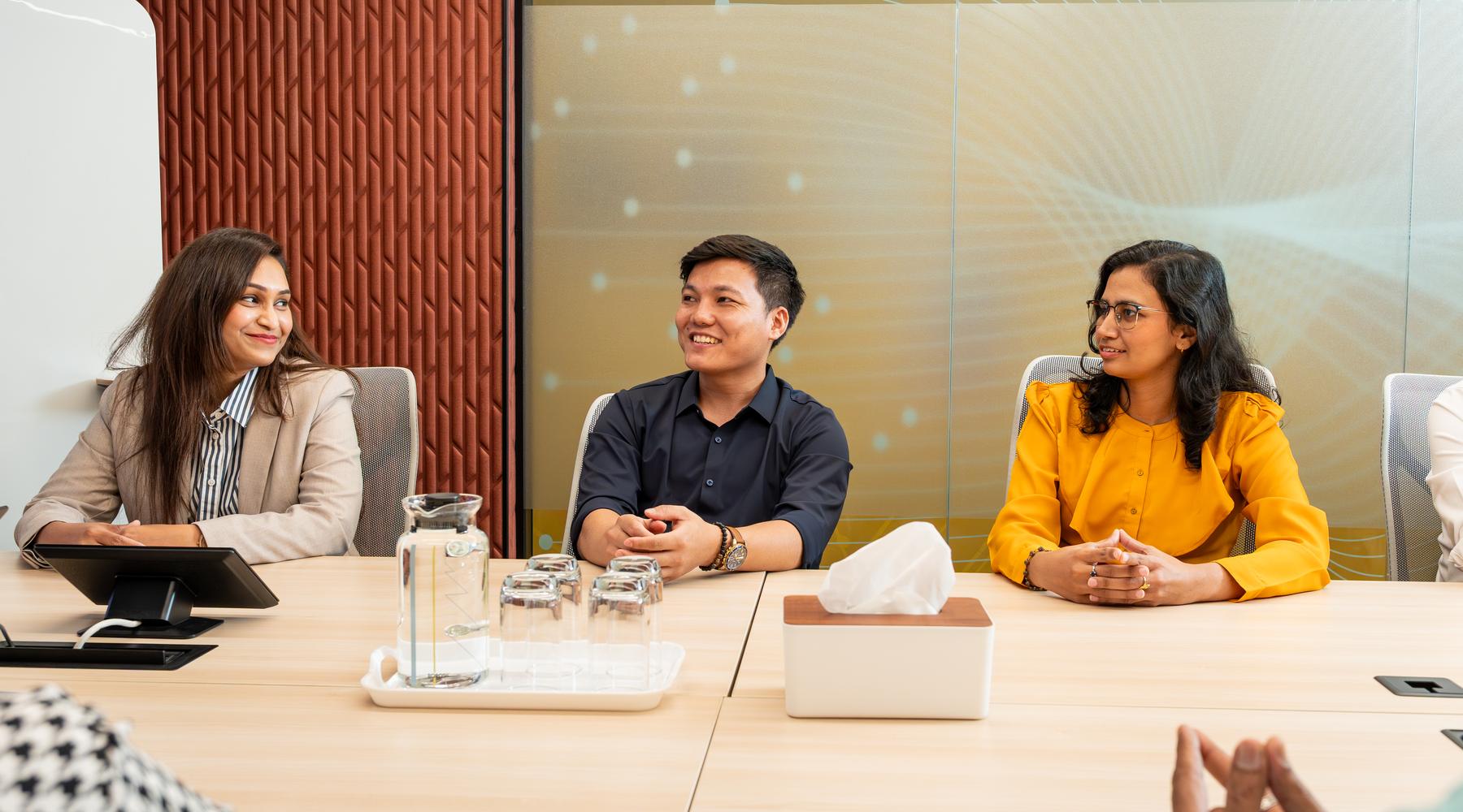 Colleagues smiling during a team discussion around a meeting table